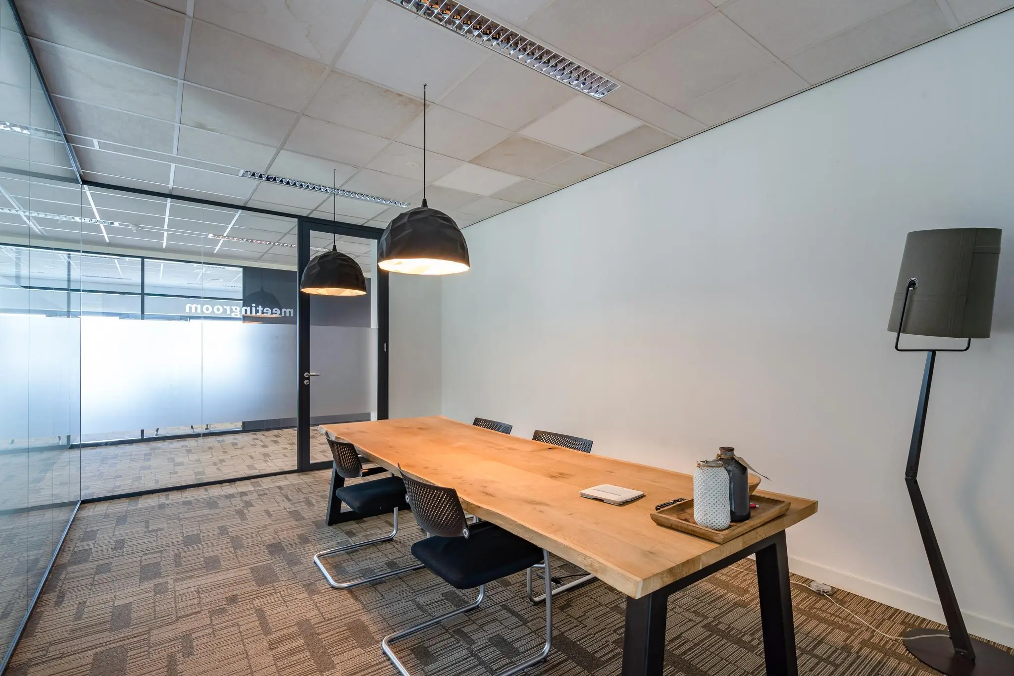 Vergaderruimte met een houten tafel, zwarte stoelen en moderne verlichting in een kantoor aan het Rivium Boulevard.
